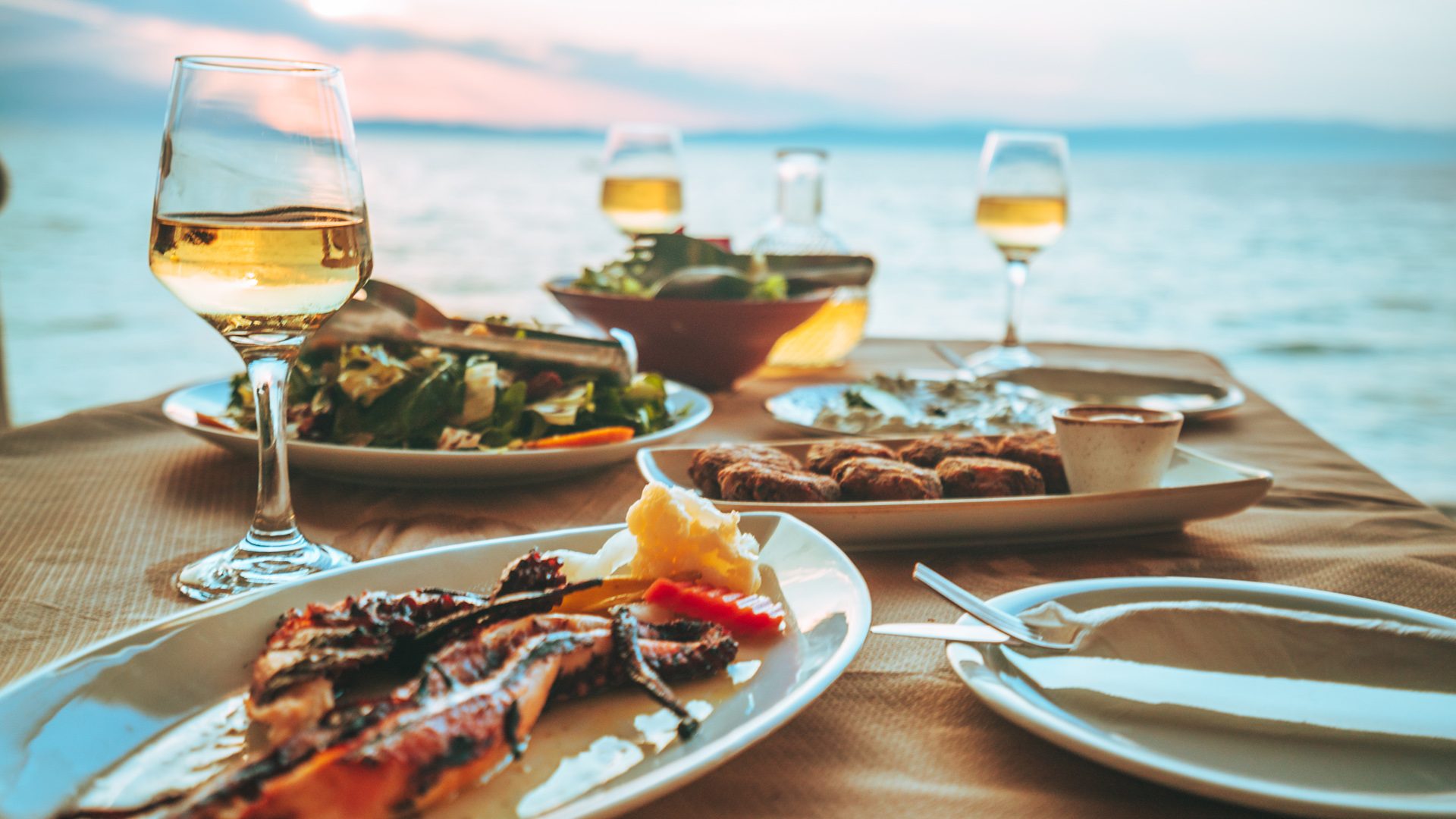 Seaside taverna table with octopus, salad and wine at sunset